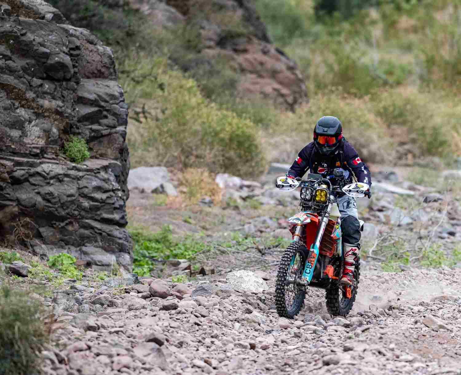 A rider on a KTM dirt bike picking a line through a rocky arroyo in the Baja desert