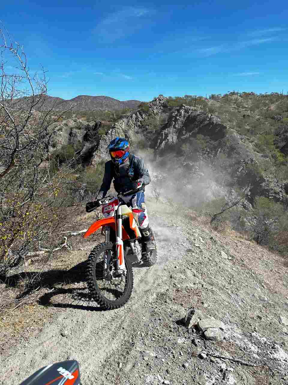 A rider on a KTM dirt bike climbing a dusty ridge track in the Baja mountains
