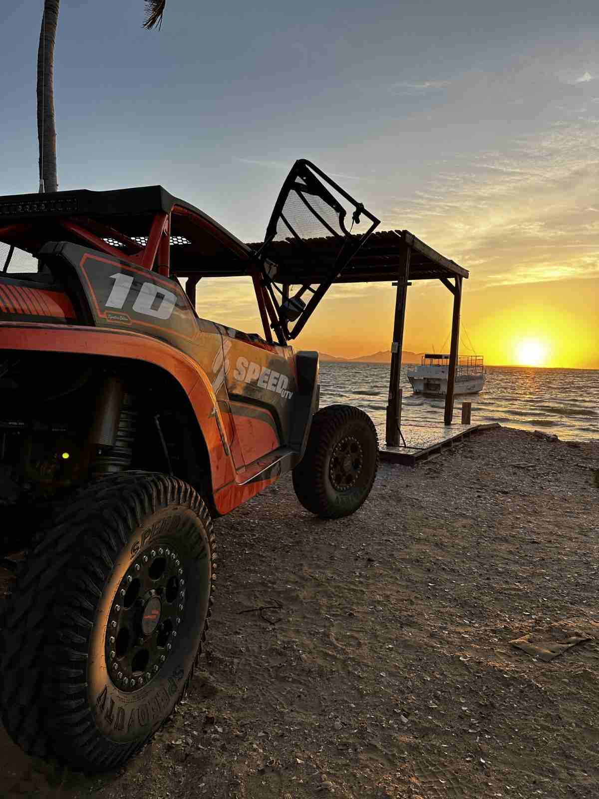An orange Speed UTV parked on the shore at sunset during a 3 day UTV expedition, with a panga moored off the beach in San Carlos, Baja