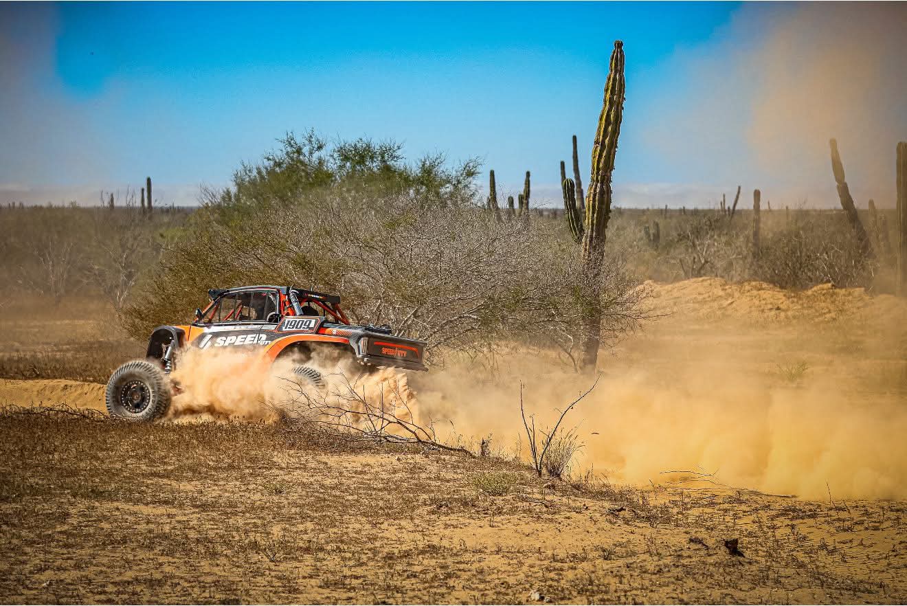 A speed UTV on a Baja desert and dust behind and cardón cactus